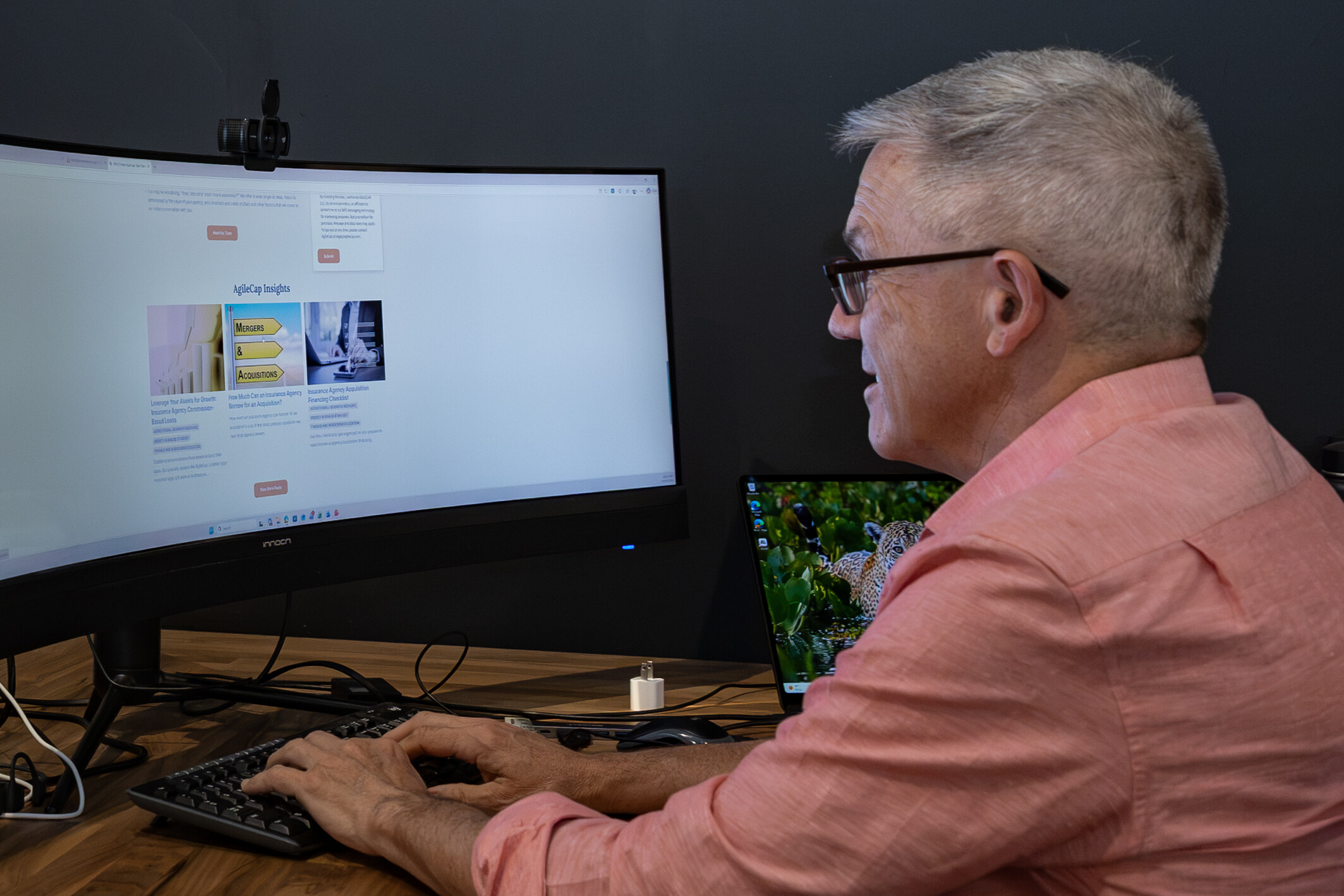 A man works on a computer, viewing a webpage on mergers and acquisitions.